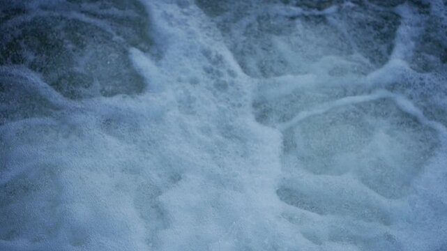 Slow motion view of water rushing over weir forming small waterfall with foam and strong aeration patterns