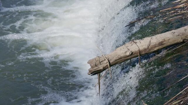 Water flows over a river weir forming a small waterfall with foam and aeration captured in slow motion detailed water movement