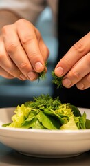 Close-up of a fair-skinned adult chef adding fresh dill herbs to a vibrant green salad in a professional kitchen bowl.