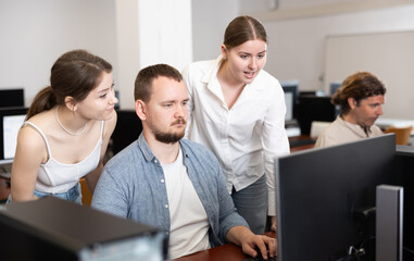 Obraz premium Two female friend companions of computer courses helps man student to figure out with performance of difficult task, master ark. Mentor observes students studies, looks at monitor screen.
