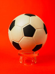 Naklejka premium Classic soccer ball rests on glass stand. Bright red background adds bold contrast. Surface texture shows subtle wear and shine. Clean composition ideal for sports or design use