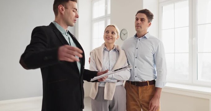 Realtor guides couple on apartment tour. The agent presents property during a showing to help buyers compare sale and rent options in a bright room. Clear real estate decision concept.