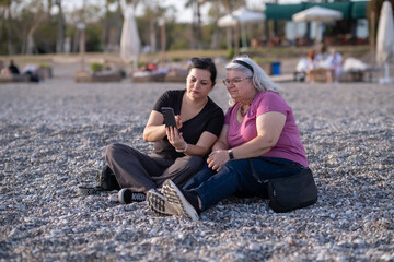 Fototapeta premium Mother and Daughter Enjoying Time Together on Beach. Senior Woman and Young Woman Having Fun at Seaside. Two Women Laughing and Relaxing on Sandy Beach. Joyful Women Spending Quality Time by the Sea.