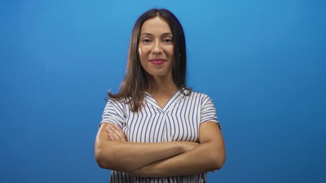 Woman with arms crossed showing bare forearms and folded hands in studio against bright blue backdrop; confidence empowerment.