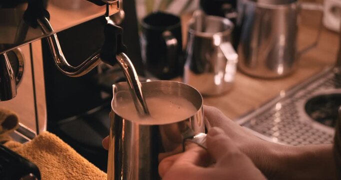 Barista frothing milk with steam wand on coffee machine in bakery cafe