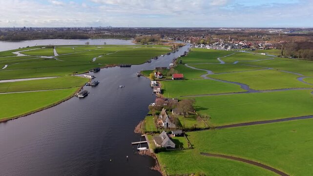Stunning aerial view of the Dutch countryside featuring interconnected canals, lush green polders, and waterfront houses. High-angle drone shot of a peaceful waterway landscape in the Netherlands.