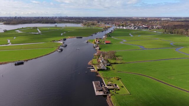 Aerial drone view of a classic Dutch water landscape with rowing boats, houseboats, and green polders. A picturesque scene of the Netherlands river system and rural architecture on a sunny day.