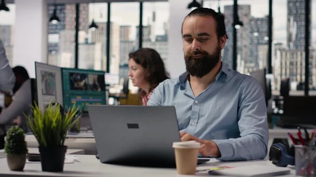 Portrait of young man staff member sitting inside open space smart office, creative agency worker planning strategy for administration and startup management. Consultant at office desk.