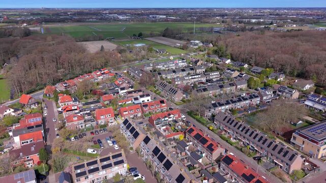 Aerial drone view of a sustainable Dutch neighborhood with solar panels on rooftops, red brick houses, and green surroundings. High angle perspective of a modern residential area in the Netherlands.