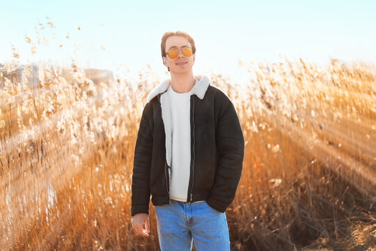 A happy young man enjoys the first warm day of spring outdoors among golden reeds. He smiles, finding peace, mental relaxation, and a social media detox in tranquil nature.