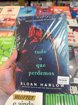 BELO HORIZONTE, MG, BRAZIL, MARCH 31, 2026. A hand holds the poignant novel "All That We Lose" by Sloan Harlow, featuring a dramatic burning rose on its dark cover.
