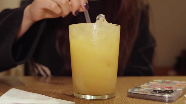 Detalle de mano femenina con u&ntilde;as decoradas sosteniendo un popote en un vaso con hielo.