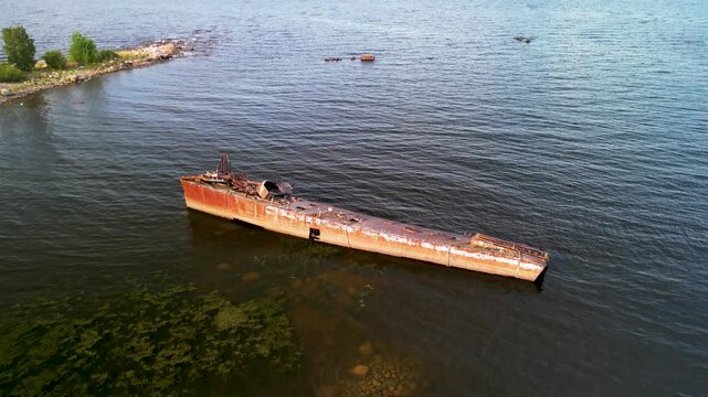Aerial pull-away from a rusty sunken shipwreck. Cinematic 4K drone footage of an abandoned ship graveyard in the water.