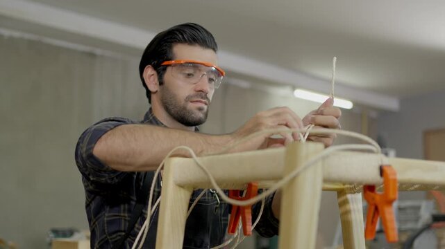Carpenter workshop safety glasses wood clamp tool artisan craftsmanship repair, worker adjusting bright work light, assembling wooden frame with hand tool for furniture construction, indoor