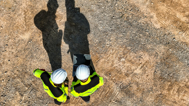 Drone perspective of male civil engineers wearing hard hats and reflective vests. Professional team inspecting the construction site ground and planning infrastructure development.