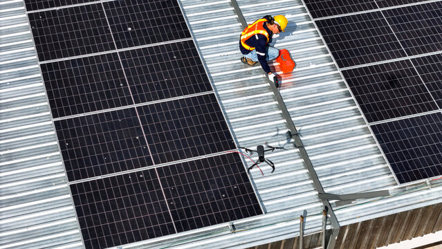 A worker wearing safety gear installing solar panels on a rooftop with nearby housing units in the background, emphasizing renewable energy, sustainability, and efficient solar power implementation