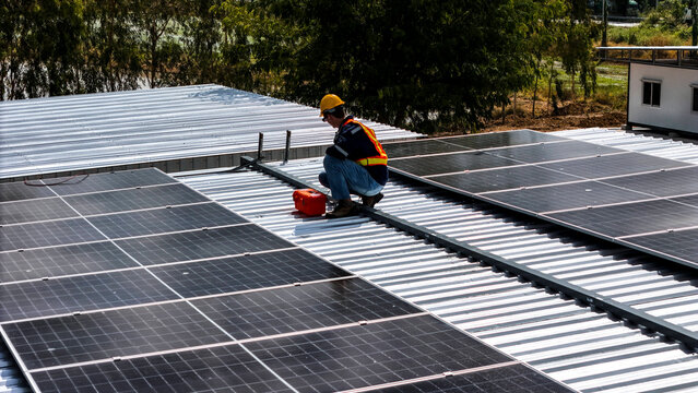 A worker wearing safety gear installing solar panels on a rooftop with nearby housing units in the background, emphasizing renewable energy, sustainability, and efficient solar power implementation