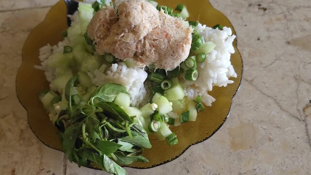 Traditional Indonesian daily meal featuring white rice topped with spiced grated coconut geneman, served with fresh cucumber and basil.