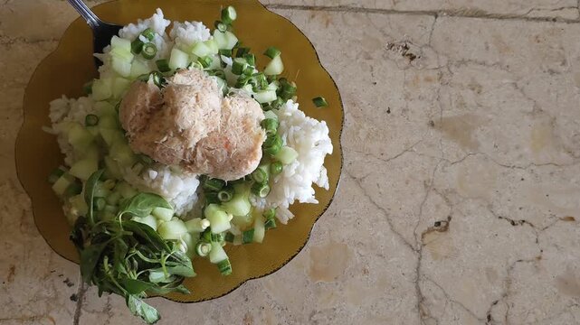 Traditional Indonesian daily meal featuring white rice topped with spiced grated coconut geneman, served with fresh cucumber and basil.