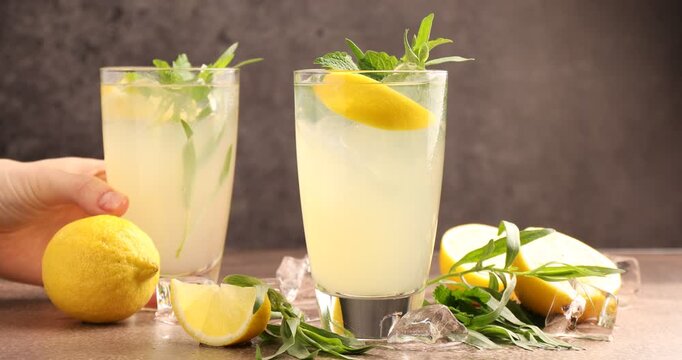 Woman putting tasty lemonade with tarragon onto grey table, closeup