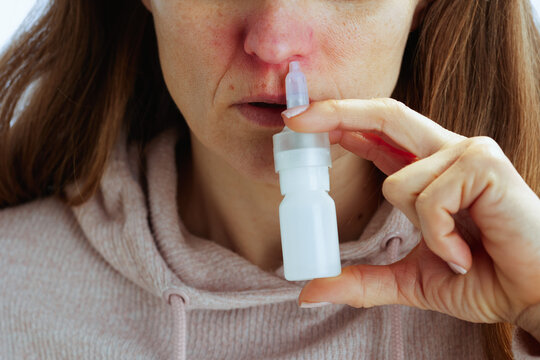 A woman in a pink hoodie uses a nasal spray bottle to find relief from sinus pressure and seasonal allergies, highlighting personal health management.