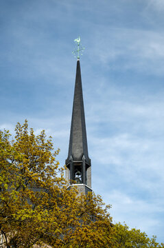 Close-up of the slender spire and green weather vane of the historic Minoritenkirche (Minorite Church) in Cologne, Germany, against a blue sky