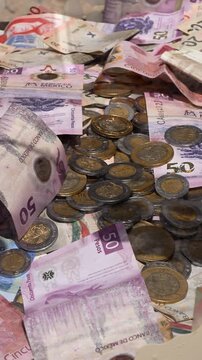 Traditional Mexican bimetallic coins scattered with banknotes inside a plastic deposit