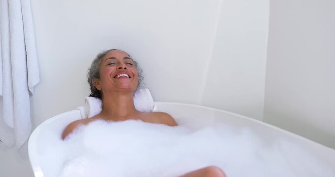 Senior African American woman relaxing in freestanding tub, smiling, breathing, knee nudging foam