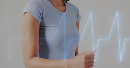 Showing mid adult woman wearing light blue tee moving arm in studio, with EKG waveform overlay © vectorfusionart