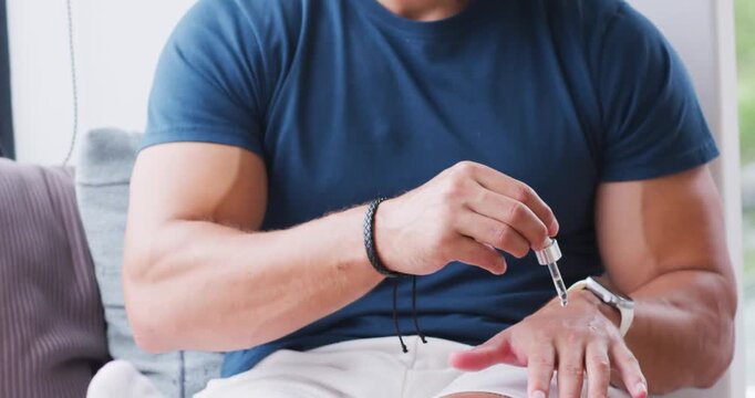 Man placing dropper, dispensing liquid onto left hand near watch and rubbing for skincare on couch