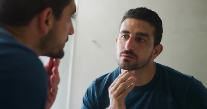 Noticing stubble in mirror, man checking beard line in bath, cupping chin with watch