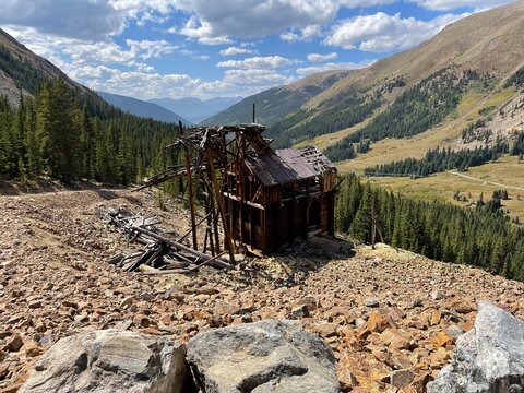 Abandoned mine headframe ruins on rocky talus slope overlooking glacial valley in Colorado Rocky Mountains
