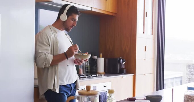 Adult man standing kitchen sun drawing glance eating cereal with spoon with headphones, copy space