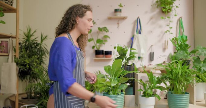 Nonbinary caretaker wearing blue top, apron, lifting green pot, arranging plants at round table