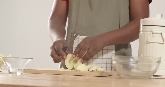 African American man in green apron slicing apples at counter with paring knife on cutting board