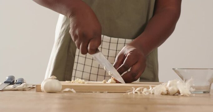 African American man holding garlic clove, peeling and mincing on board with knife, preparing meal