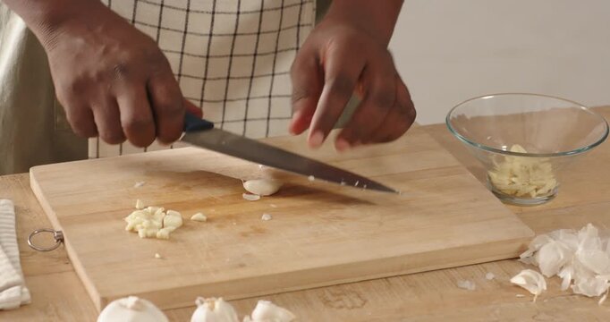 African American man peeling slicing mincing garlic for cooking on board with blue knife in apron