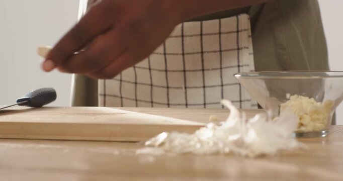 African American man in checked apron peeling and slicing garlic at home counter with chef's knife