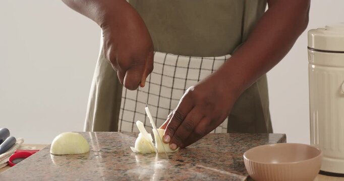 Midadult African American steadying halved onion on speckled counter slicing with knife for meal