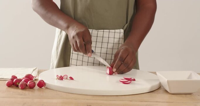 African American man reaching for radish, steadying-slicing with knife on counter for dish apron
