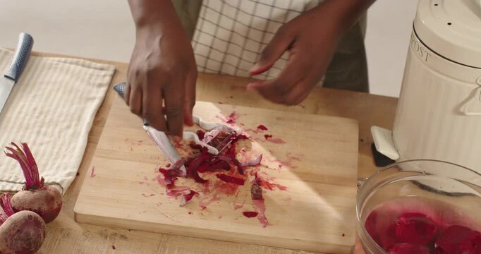 African midadult male holding beet peeling at kitchen on board with peeler cutting with blue knife