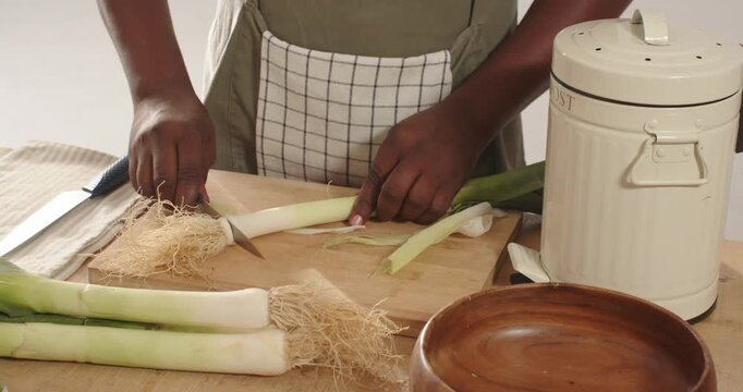 African American man picking leek trimming roots slicing with knife at kitchen counter for cooking