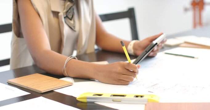 African American woman consulting tablet guiding marking plans with yellow pencil at studio desk