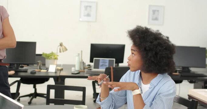 Diverse female coworkers discussing samples at round table while seated colleague pointing swatches