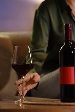 Woman taking glass of red wine from table at home late in evening, closeup