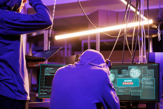 Upset hackers getting access denied message while hacking network system. Unhappy criminals breaking online server unsuccessfully on computer in abandoned warehouse at night