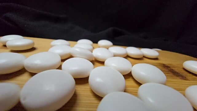 A close-up macro photograph of smooth white almond drag&eacute;e candies arranged like zen pebbles on a wooden board against a dark background.