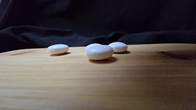 A close-up macro photograph of smooth white almond drag&eacute;e candies arranged like zen pebbles on a wooden board against a dark background.