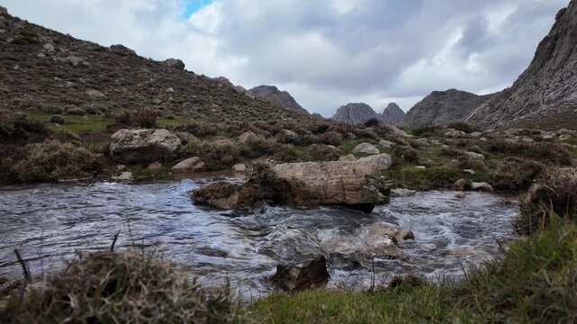 A beautiful landscape featuring a clear stream flowing over rocks in a mountainous region with rolling hills and a dramatic cloudy sky in Tikjda, Algeria