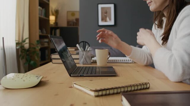 Medium close-up of young professional woman participating in video call with project team, losing broadband signal, removing earbuds, checking wifi router, removing cable and reacting with dismay
